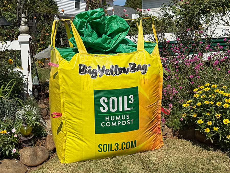 Yellow bag labeled 'Big Yellow Bag' with 'SOIL3' branding, filled with green compost, in a garden setting.