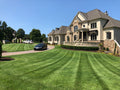 A large suburban house with a manicured Zenith Zoysia lawn in the foreground, a driveway with a black car under a clear blue sky.
